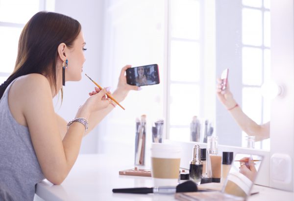 Beauty blogger filming makeup tutorial with smartphone in front of mirror .